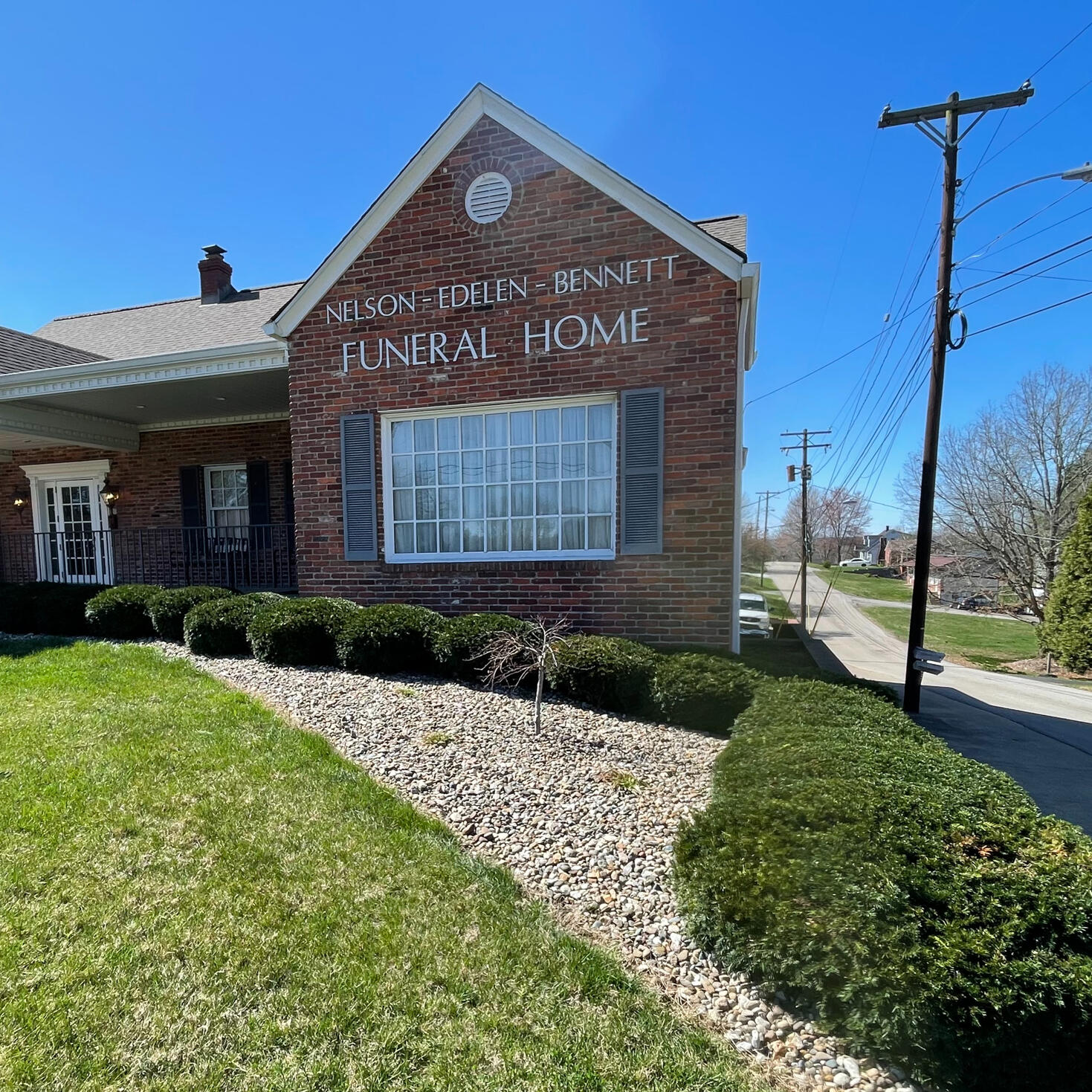 Nielson Funeral Home A large rock bed with freshly trimmed shrubs in front of a one-story, brick Funeral Home on a sunny day.