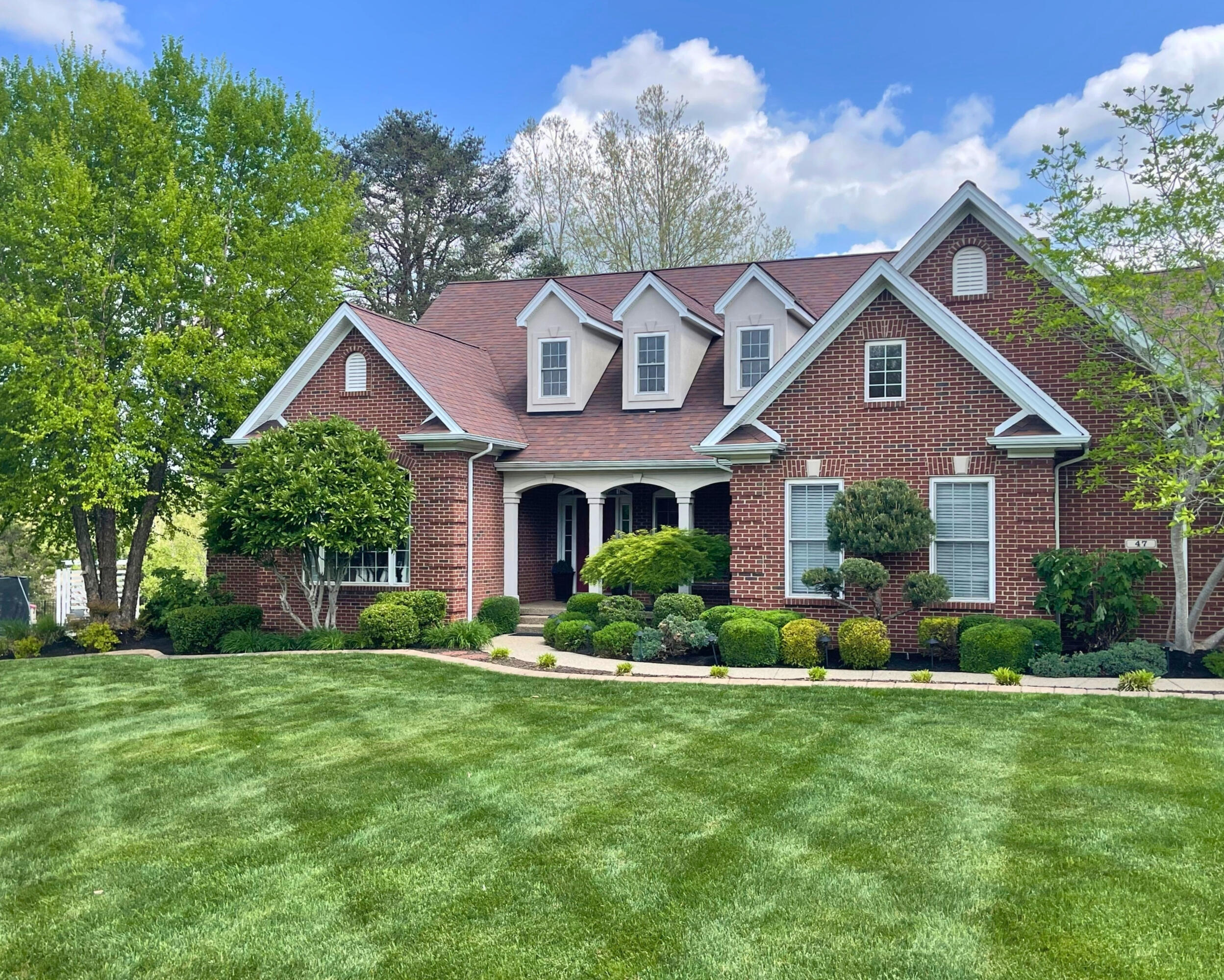 Residential Landscaping A two-story, brick home with freshly cut lawn and several shrubs and small trees in the yard.